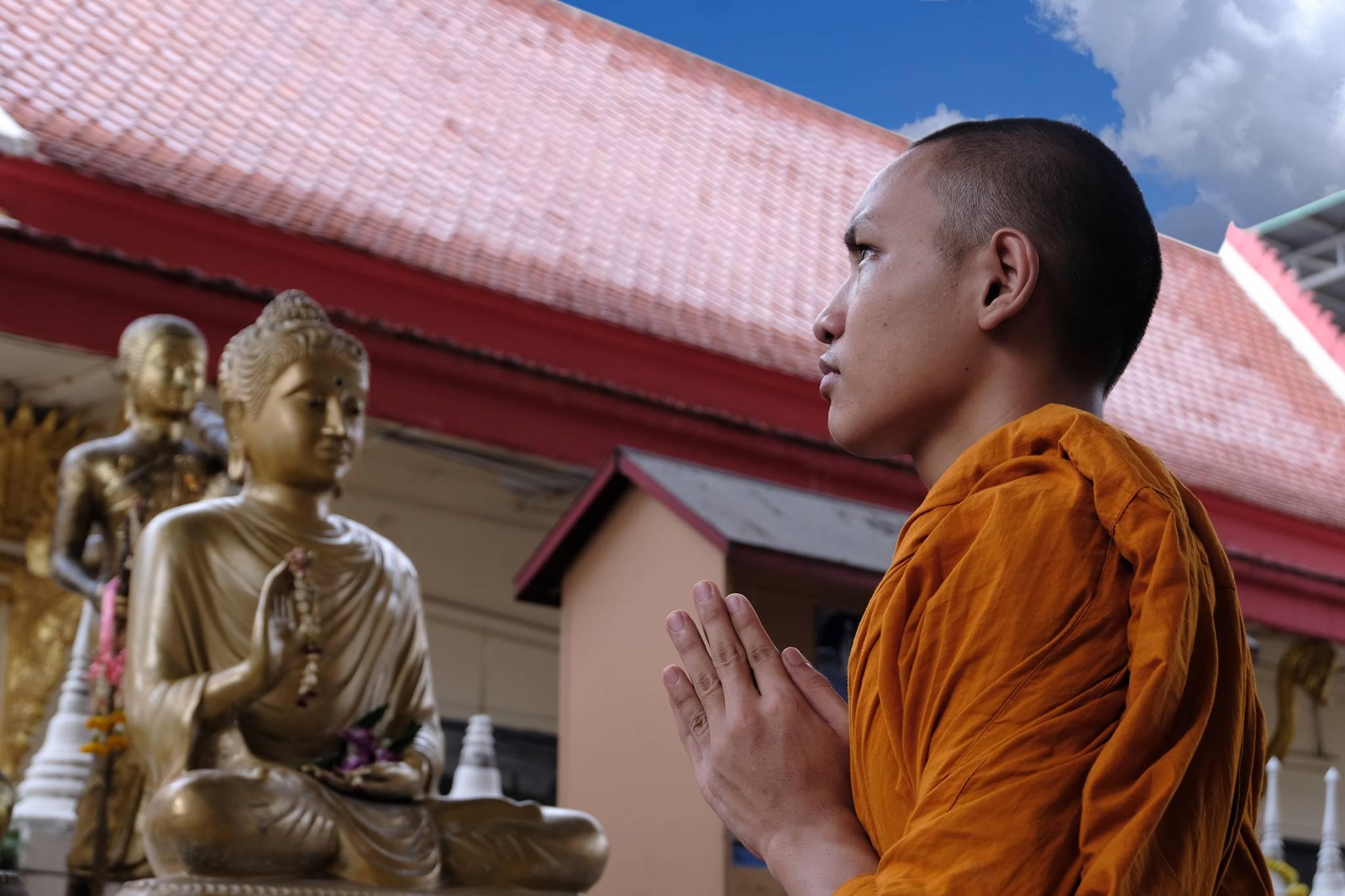 moine tibétain prie devant une statue de Bouddha