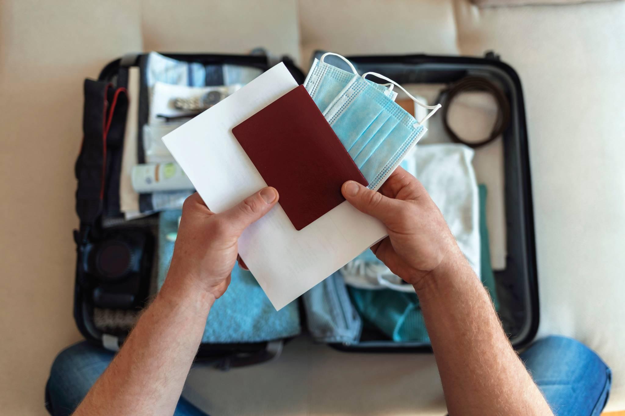 une personne prépare sa valise et tient son passeport et des masques