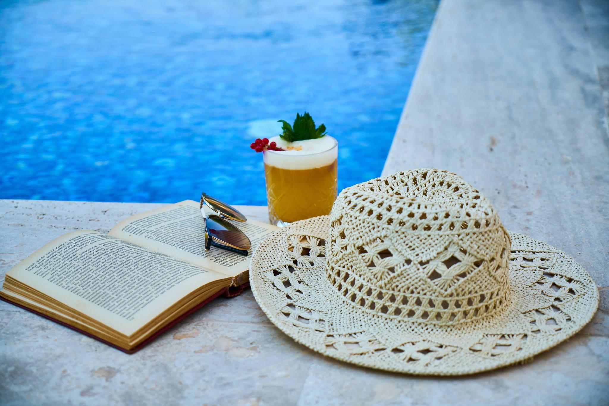 livre avec chapeau et cocktail au bord de la piscine