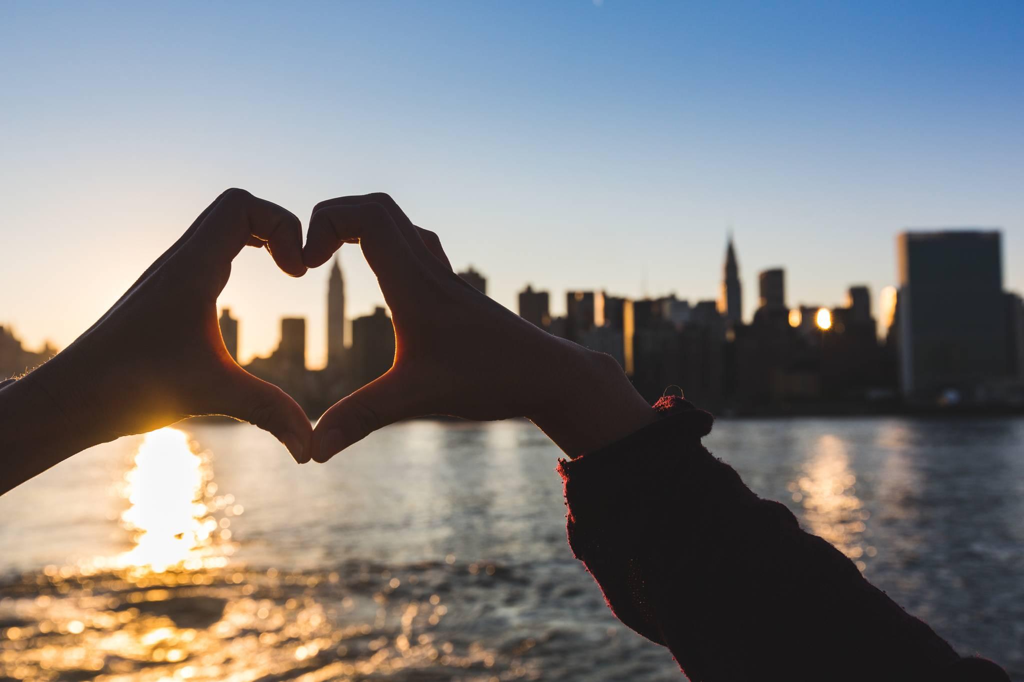 mains en forme de cœur devant la ville de New York au coucher du soleil